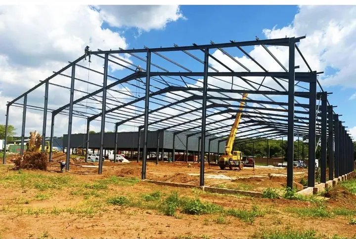 Kingson Engineering steel portal frame under erection, with columns, rafters and purlins in place and a mobile crane inside the structure.