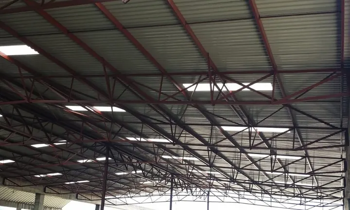 The underside of a long-span roof: red-oxide steel trusses and purlins carrying sheeting, photographed looking up along the building.